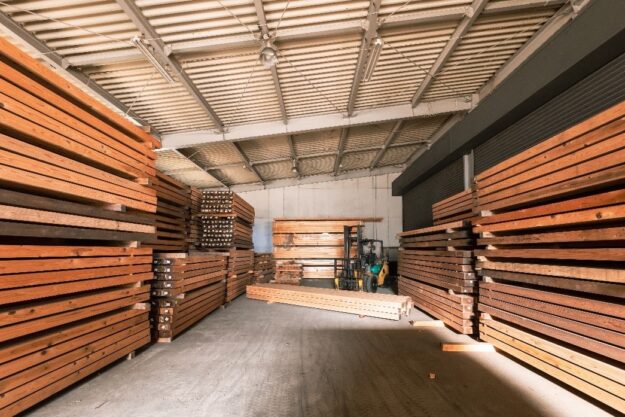 Indoor lumber storage with stacked wooden beams and a forklift in a spacious warehouse.